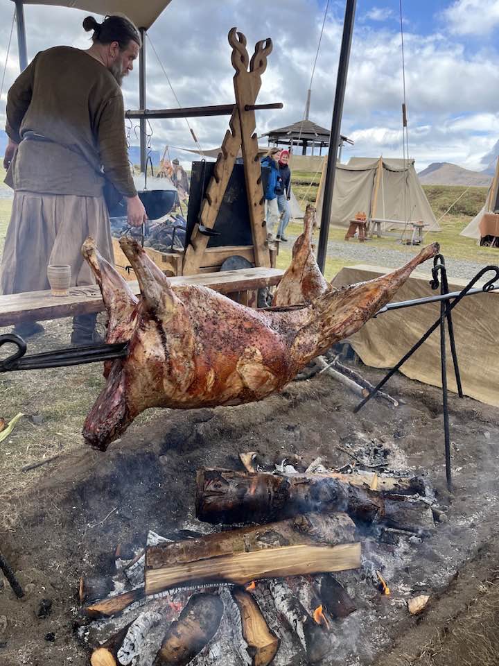Lamb í heilgrillun á víkingahátíðinni. Maður í víkingafötum stendur við eldstæði fyrir aftan.